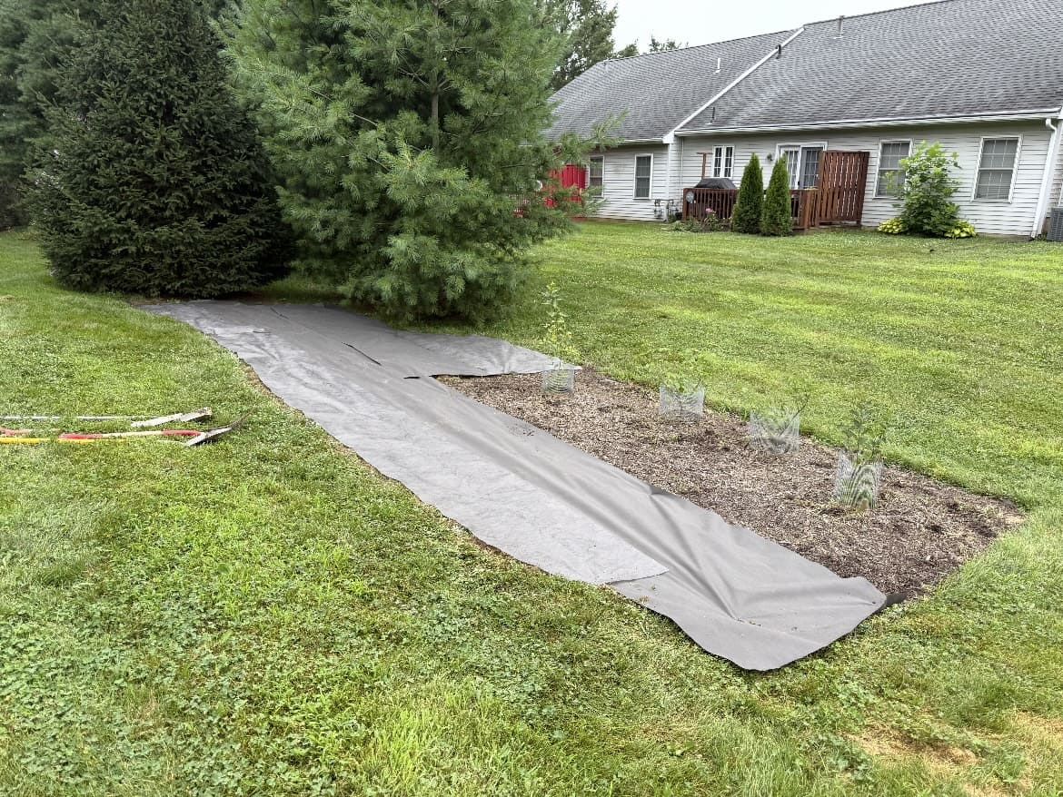 Landscape fabric laid across a garden bed beside a lawn